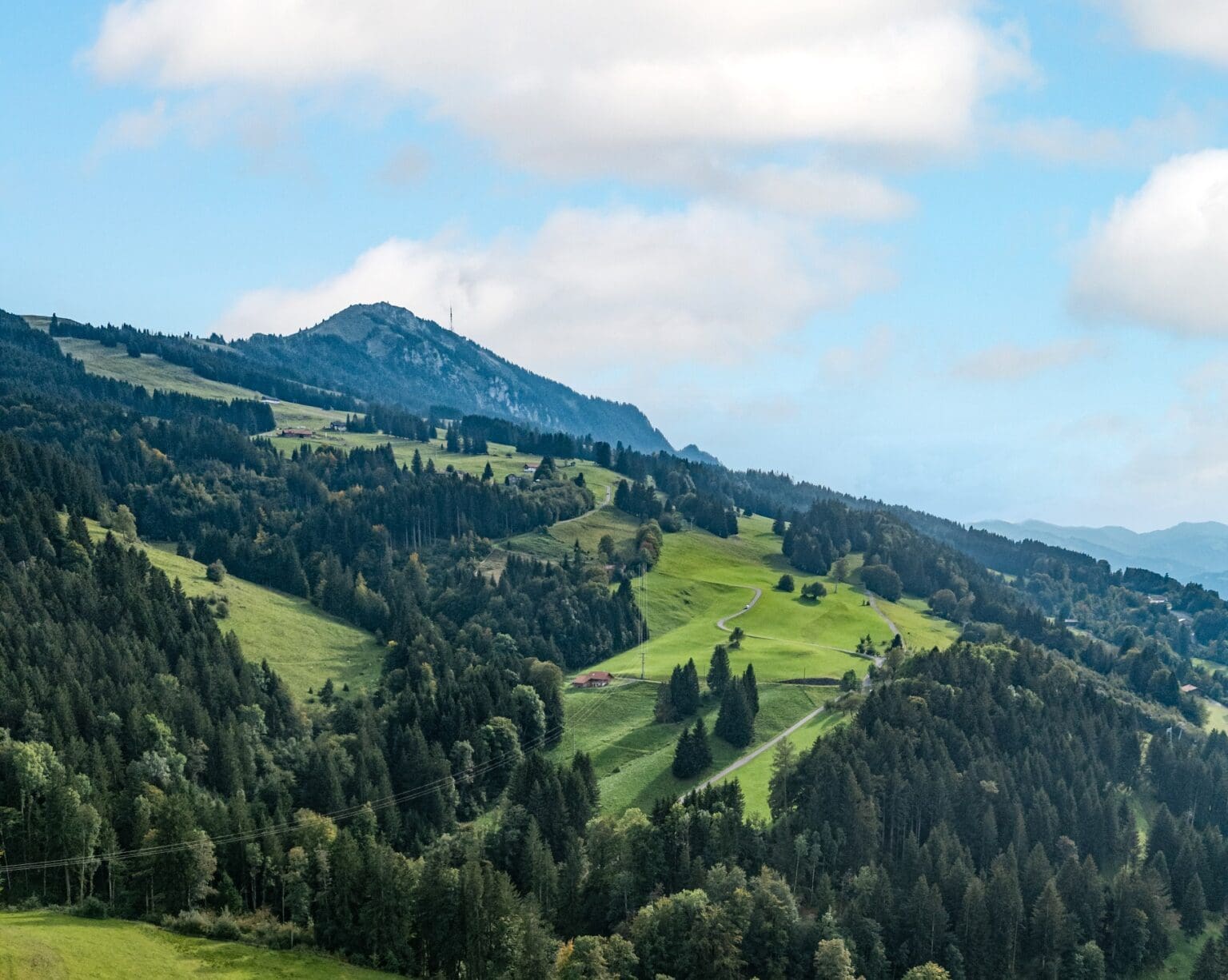 Wandern auf der grünen Wiese im bayerischen Bergland mit Blick auf den Gipfel des Hochkalters im Hintergrund, umgeben von Wäldern und landwirtschaftlichen Flächen.