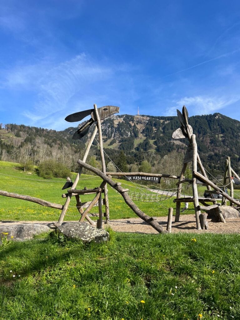 Es ist ein Spielplatz mitten in der Natur vor einem hohen Berg zu sehen.