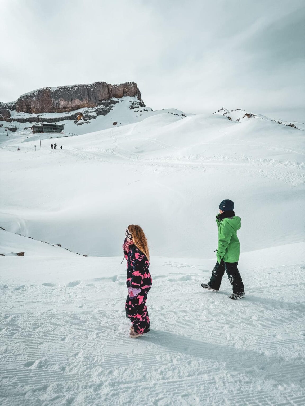 Zwei Kinder vor einem hohen Berg inmitten einer Schneelandschaft