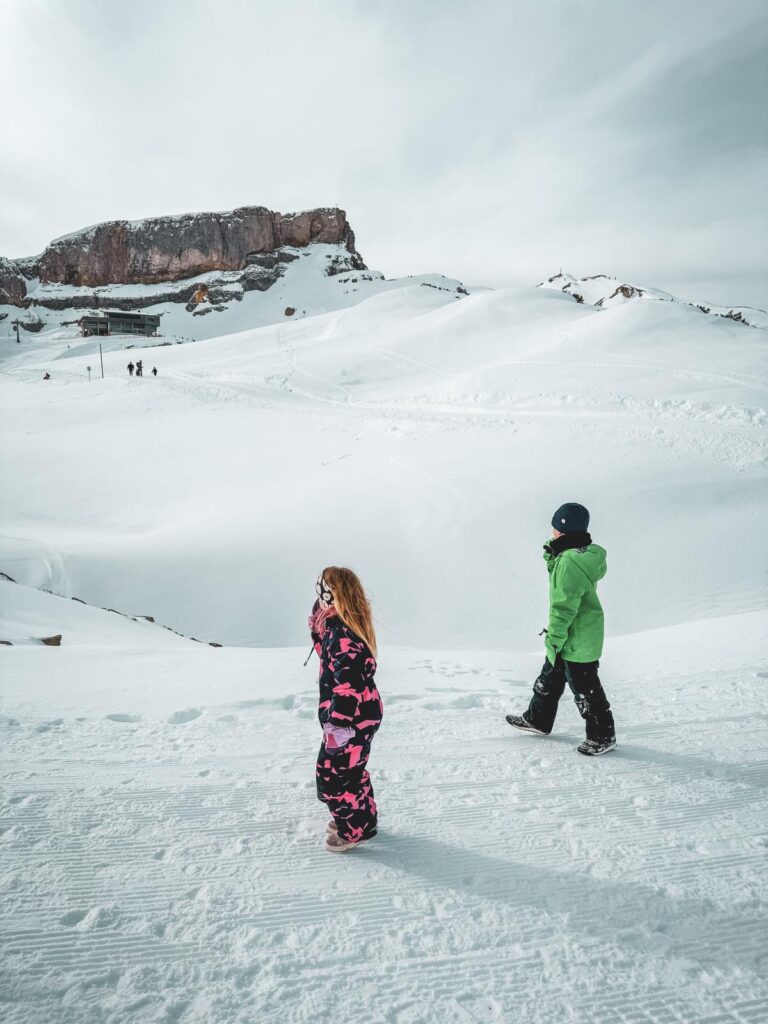 Zwei Kinder vor einem hohen Berg inmitten einer Schneelandschaft